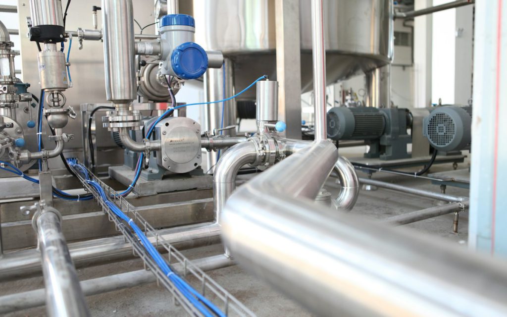 Stainless steel process piping with pumps and valves on a plant floor