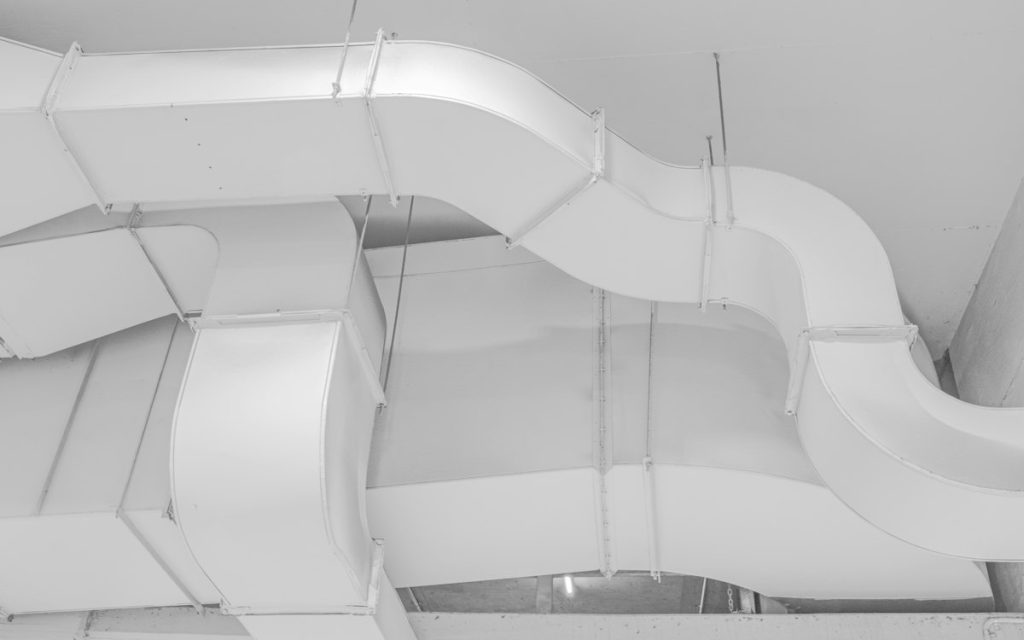 White rectangular and round ductwork running along a ceiling