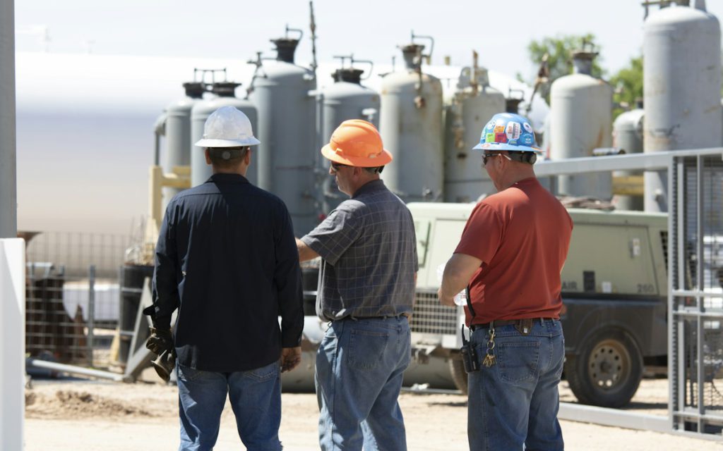 Three workers in hard hats discussing equipment at an industrial site