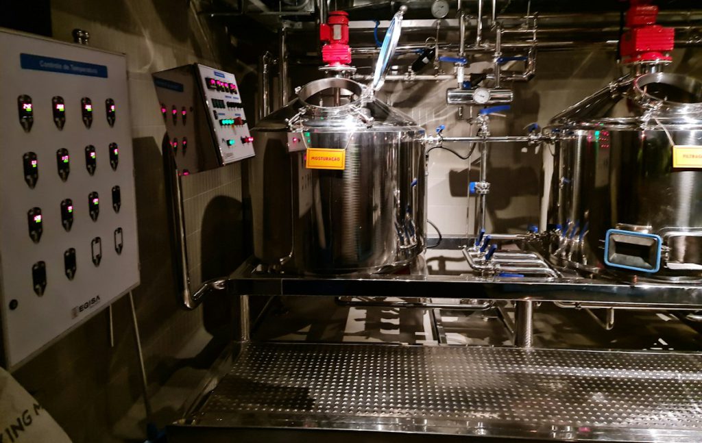 Stainless brewhouse tanks and piping beside a control panel