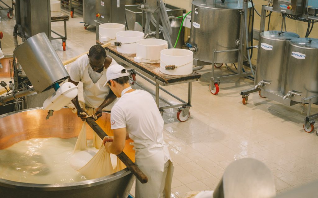 Workers in white uniforms and caps at stainless steel vats in a dairy plant
