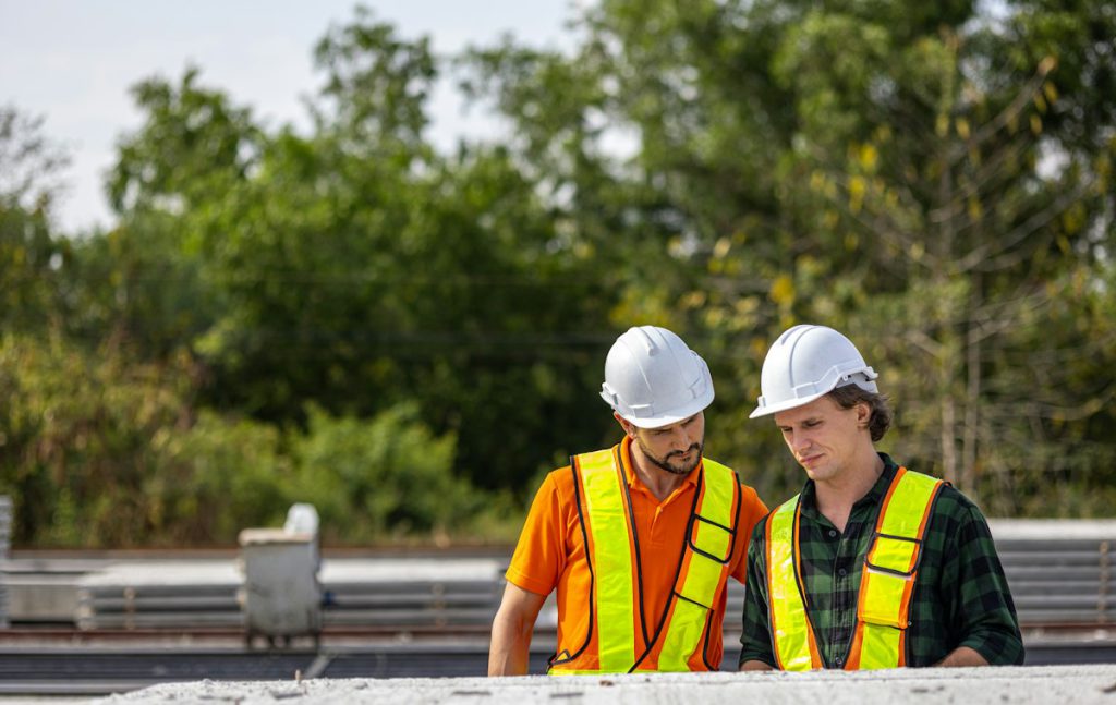 Two site engineers in hard hats and high-visibility vests checking work outdoors