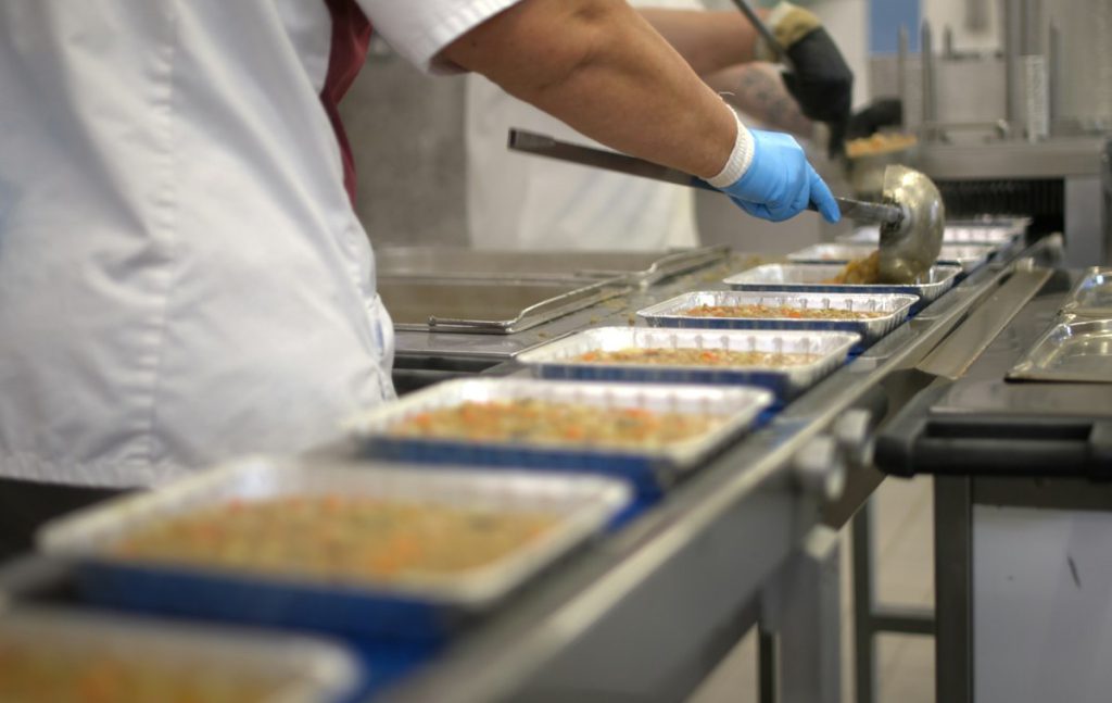 Gloved worker filling food trays on a conveyor line