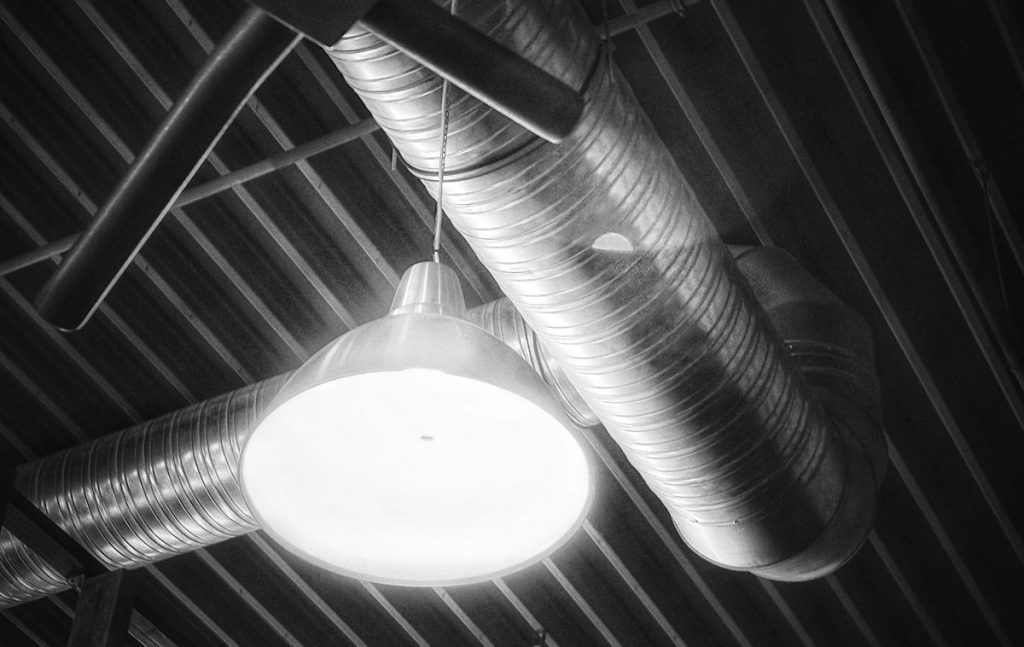 Exposed spiral ventilation duct and pendant light in an industrial ceiling
