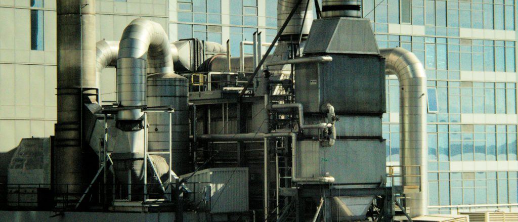 Rooftop air handling equipment and large ductwork beside a glass office building