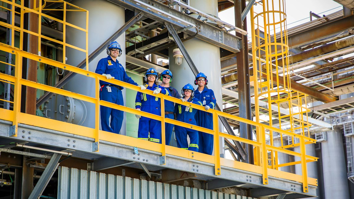 Engineering team in coveralls, hard hats and safety glasses on a platform at an industrial plant